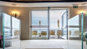 A modern hotel lobby with a glass entrance leading to a balcony with outdoor seating and a view of the sea. - Excelsior Palace Portofino Coast (Rapallo)