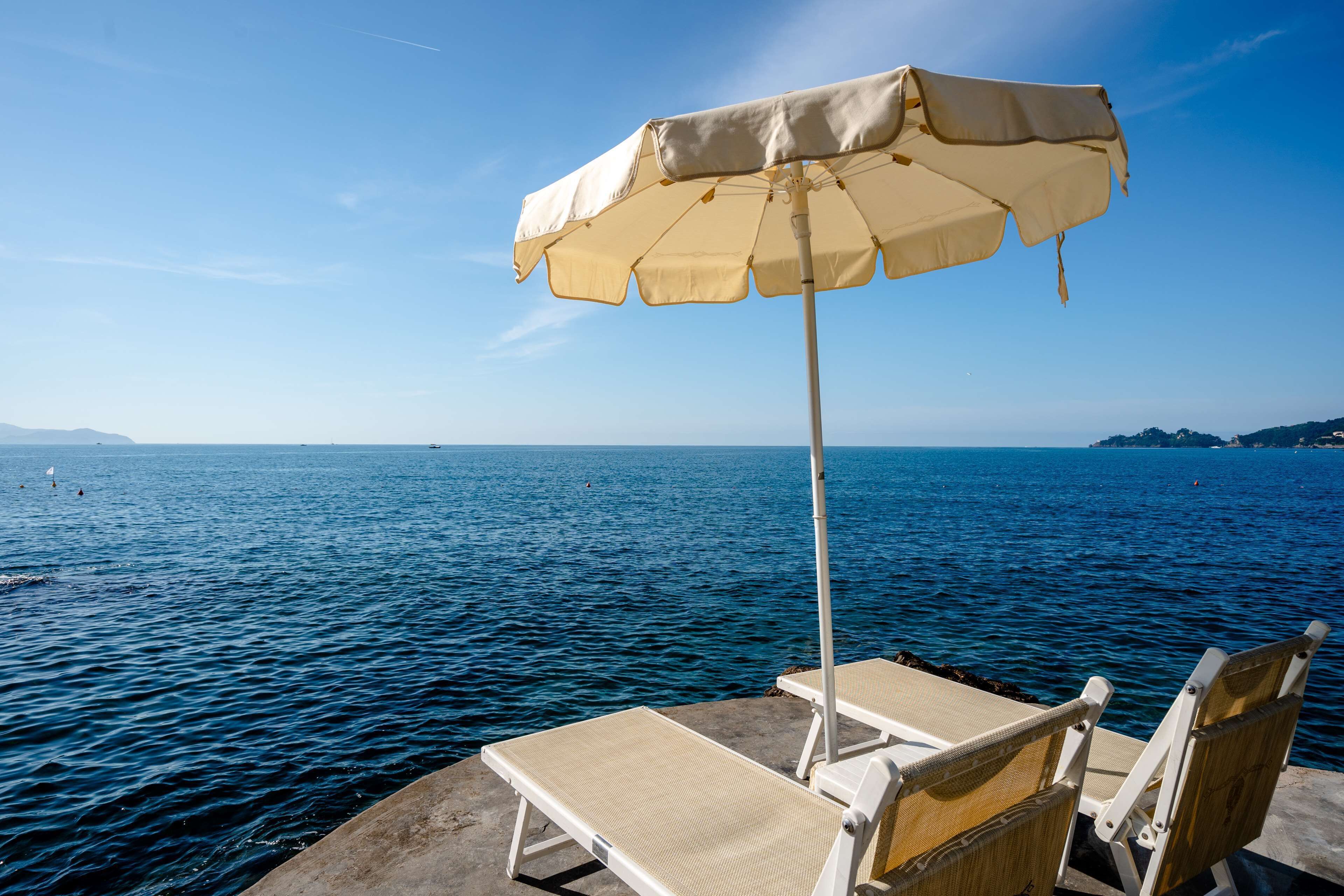Une vue sur la mer avec un parasol de plage et deux chaises longues sur une plateforme en béton.