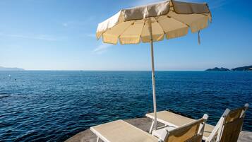 Une vue sur la mer avec un parasol de plage et deux chaises longues sur une plateforme en béton.