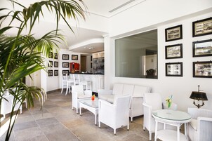 Amplia sala de estar con mobiliario de mimbre blanco, una mesa de centro de vidrio y cuadros enmarcados en las paredes.