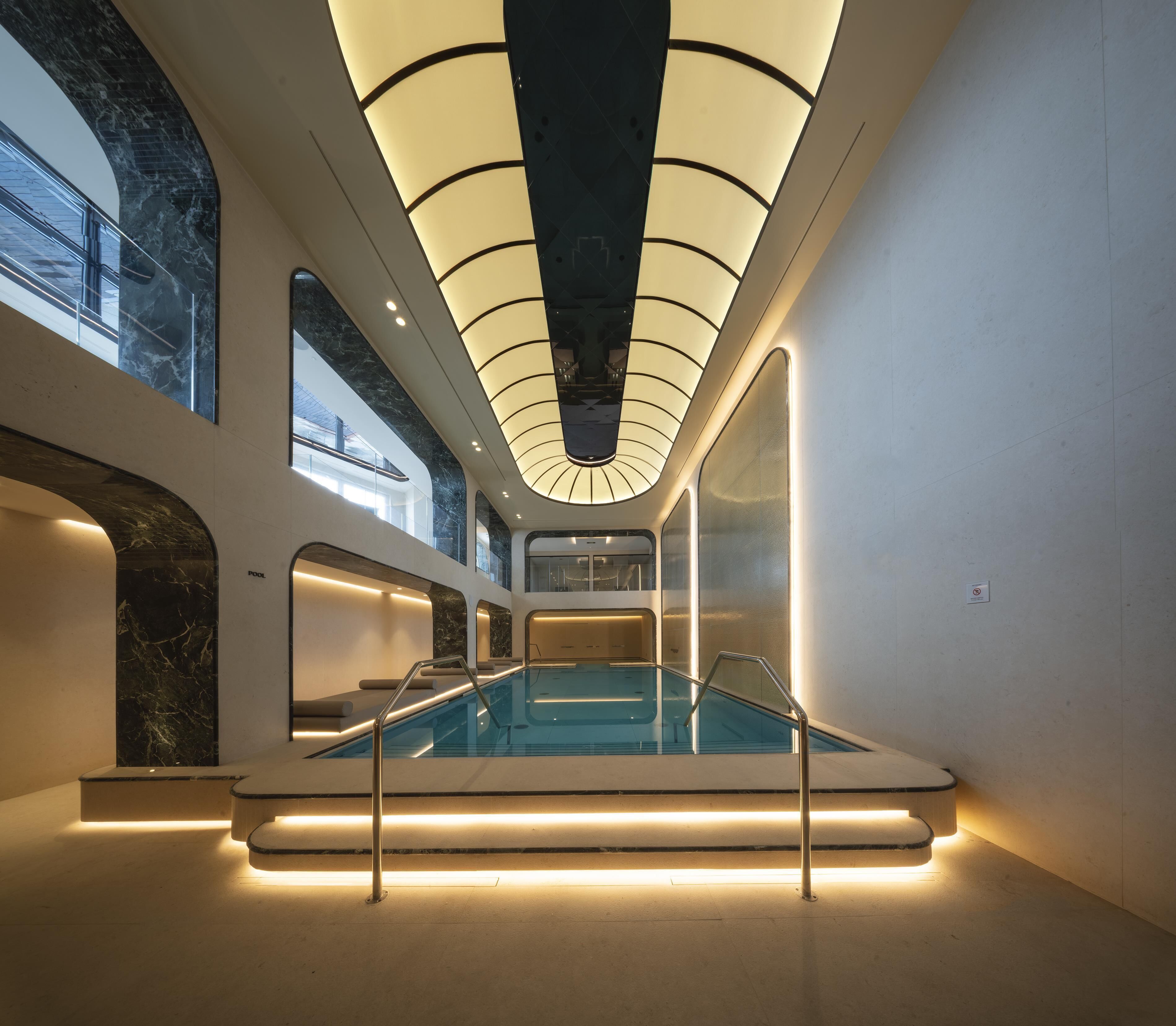 Una piscina interior moderna con barrera de vidrio y un techo con un diseño de iluminación único.