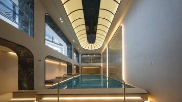 Una piscina interior moderna con barrera de vidrio y un techo con un diseño de iluminación único.