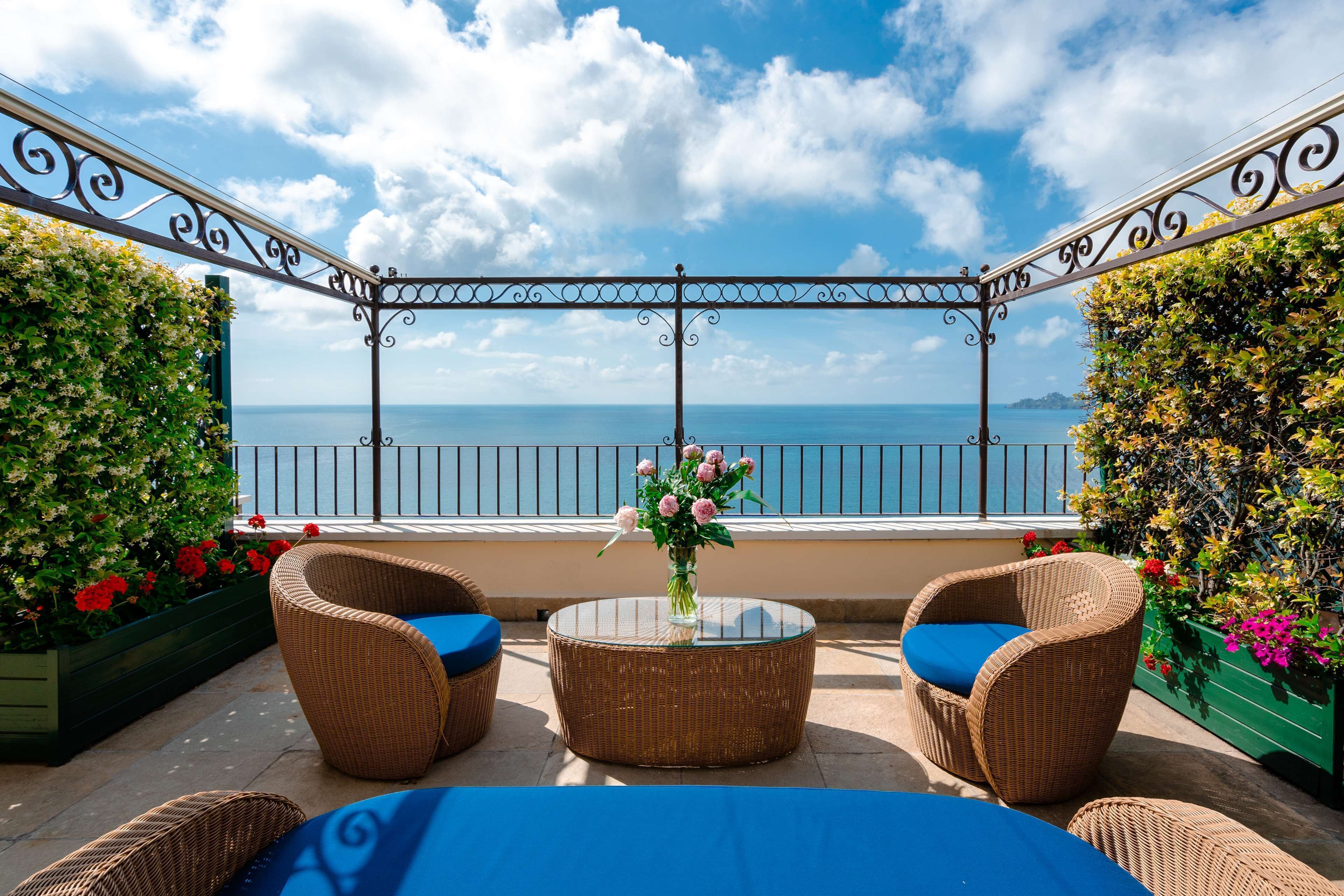 A balcony with wicker furniture, a glass table, and a vase of flowers.