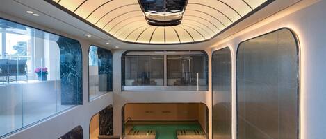Une piscine intérieure moderne dotée d’un plafond au design unique, de murs en verre et d’un espace détente.