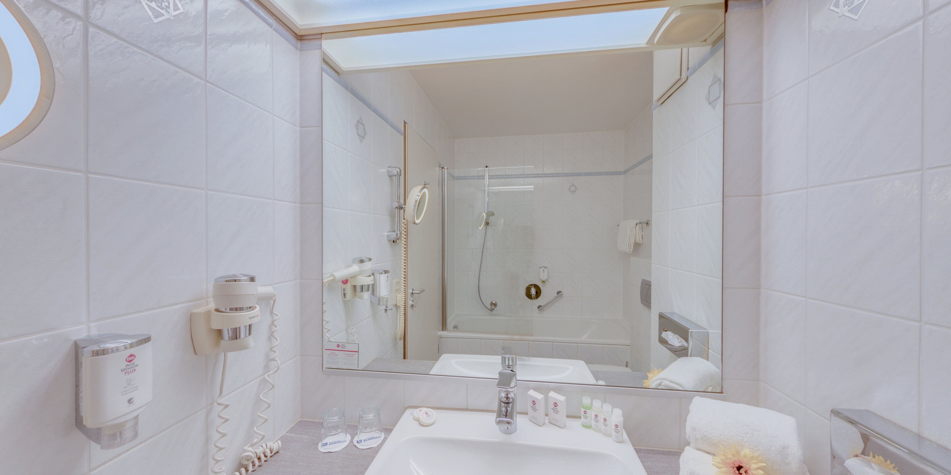 Un baño moderno con ducha de vidrio, un espejo grande y un lavabo con artículos de aseo.