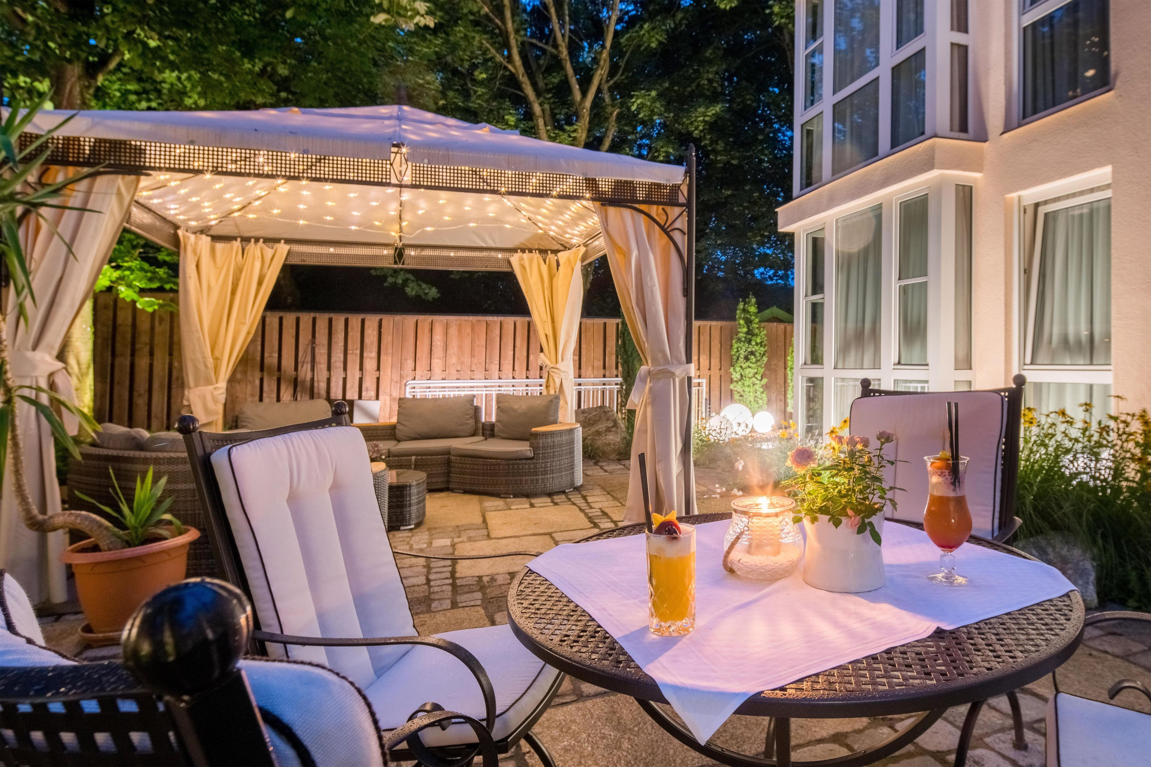 An outdoor patio area with a covered seating area, a table with drinks, and a potted plant.