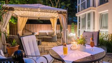 An outdoor patio area with a covered seating area, a table with drinks, and a potted plant.