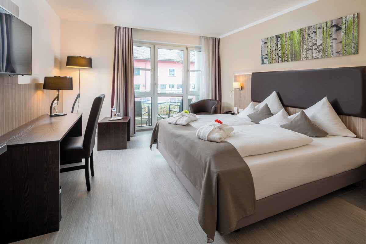 A hotel room with a bed, a desk, a chair, a TV, and a window with curtains.
