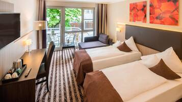 A hotel room with two beds, a desk with a chair, a TV, and a balcony with outdoor furniture.