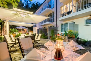 Un área de comedor al aire libre con mesas, sillas y sombrillas.