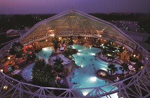 A large indoor swimming pool with multiple levels and a glass ceiling, surrounded by lounge areas and palm trees. - Best Western Plus Parkhotel Erding (Erding)