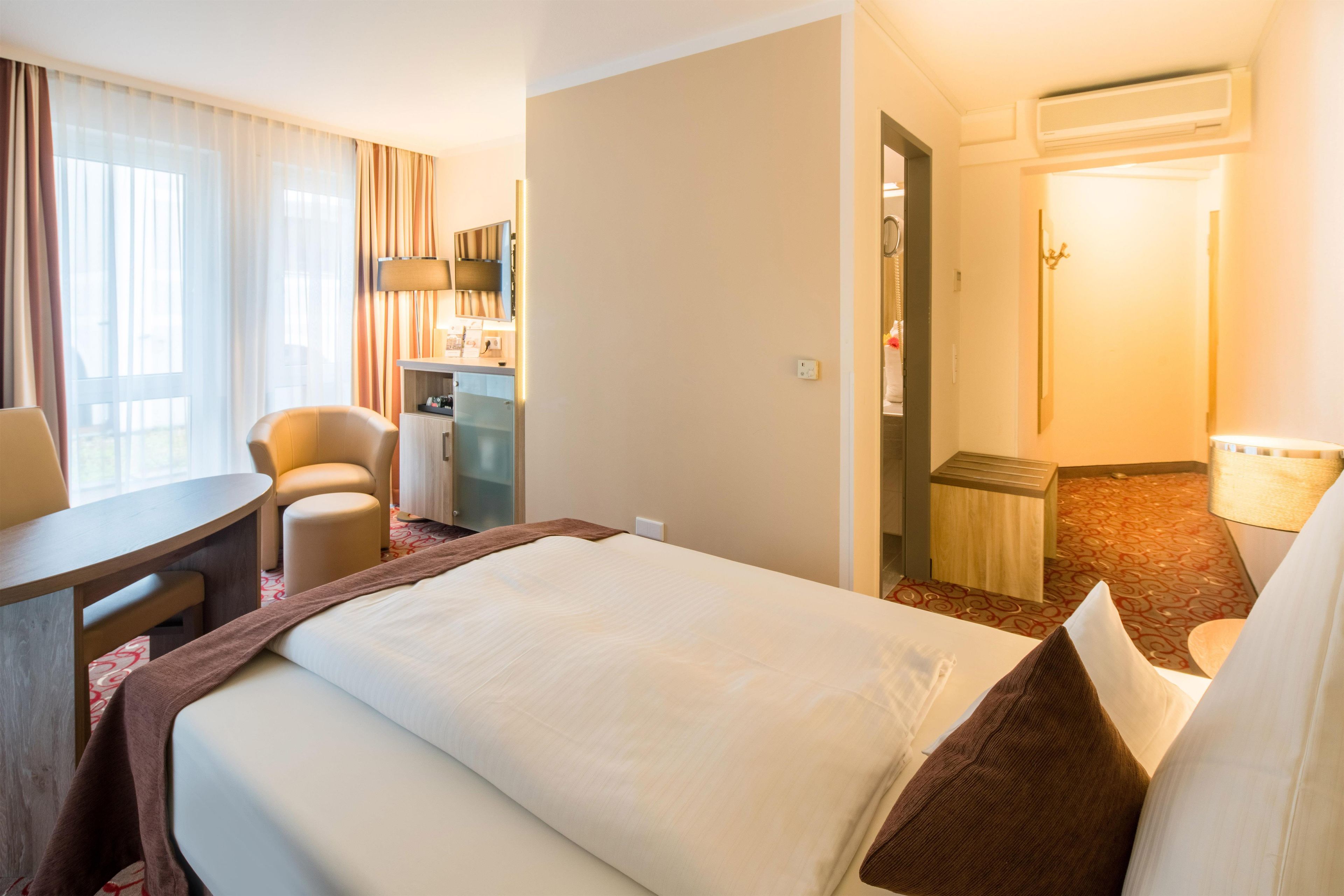 Une chambre d’hôtel comprenant un lit, un bureau, une chaise, une petite kitchenette et une salle de bain.