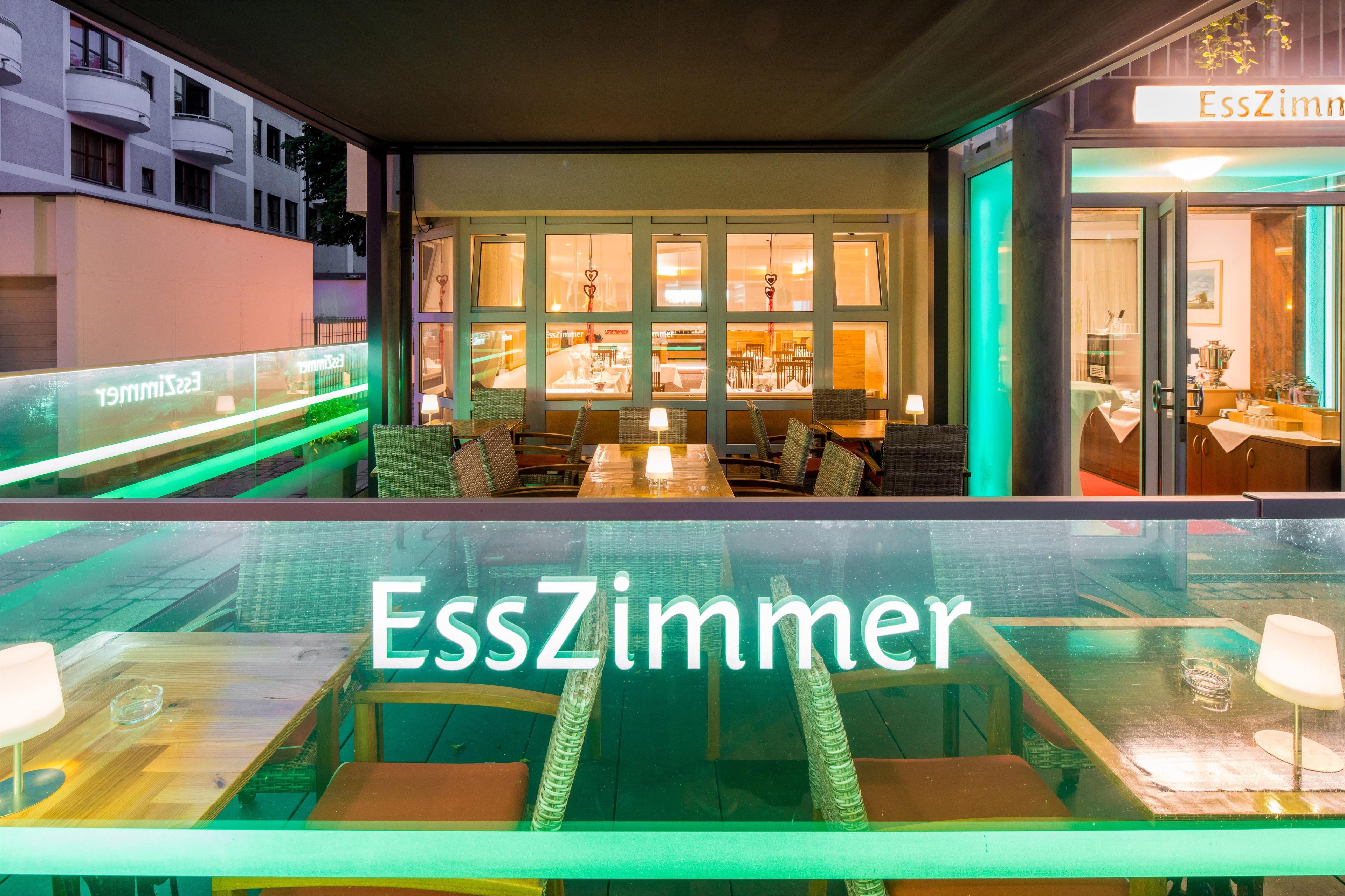 A restaurant with a view of the city, tables with chairs, and a sign reading 'EssZimmer'.