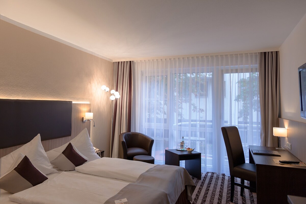 A hotel room with a large bed, two chairs, a desk, and a TV.