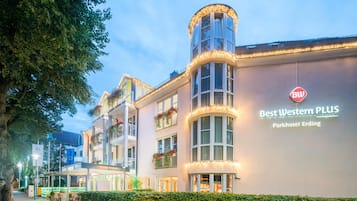 Ein Hotel mit einer Gebäudeecke im Bogen, zahlreichen Fenstern und einem Schild, das es als Best Western PLUS Parkhotel Erding kennzeichnet.