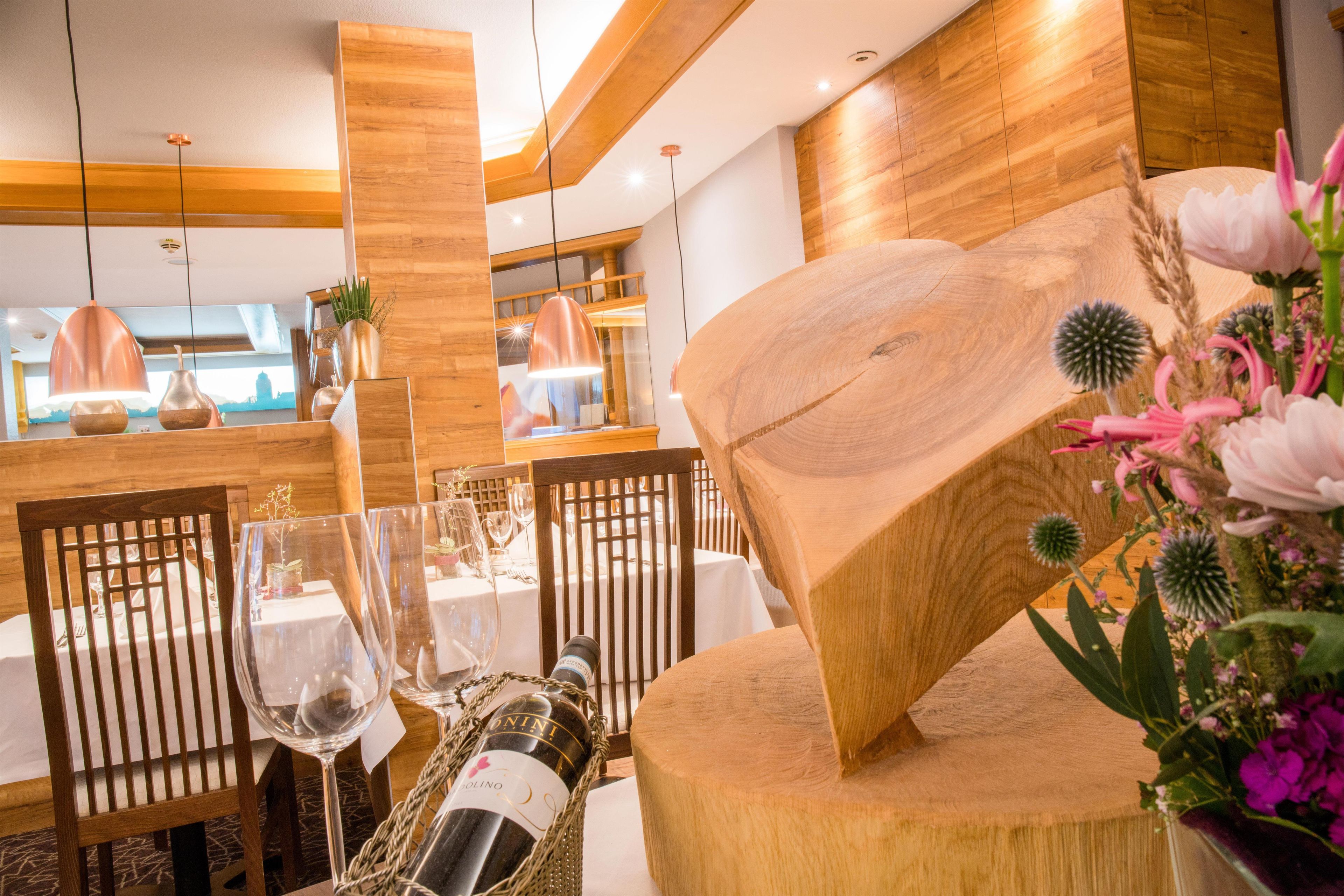 A dining area with wooden chairs, tables set for a meal, and a bottle of wine on the table.