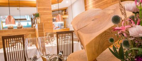A dining area with wooden chairs, tables set for a meal, and a bottle of wine on the table.