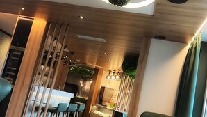 Un interior moderno con techo de madera, iluminación circular, una zona de bar y sillas tapizadas en verde.