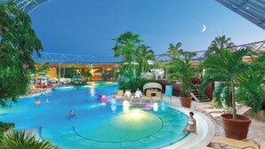 A large indoor swimming pool with multiple lanes, surrounded by lounge chairs and palm trees. - Best Western Plus Parkhotel Erding (Erding)
