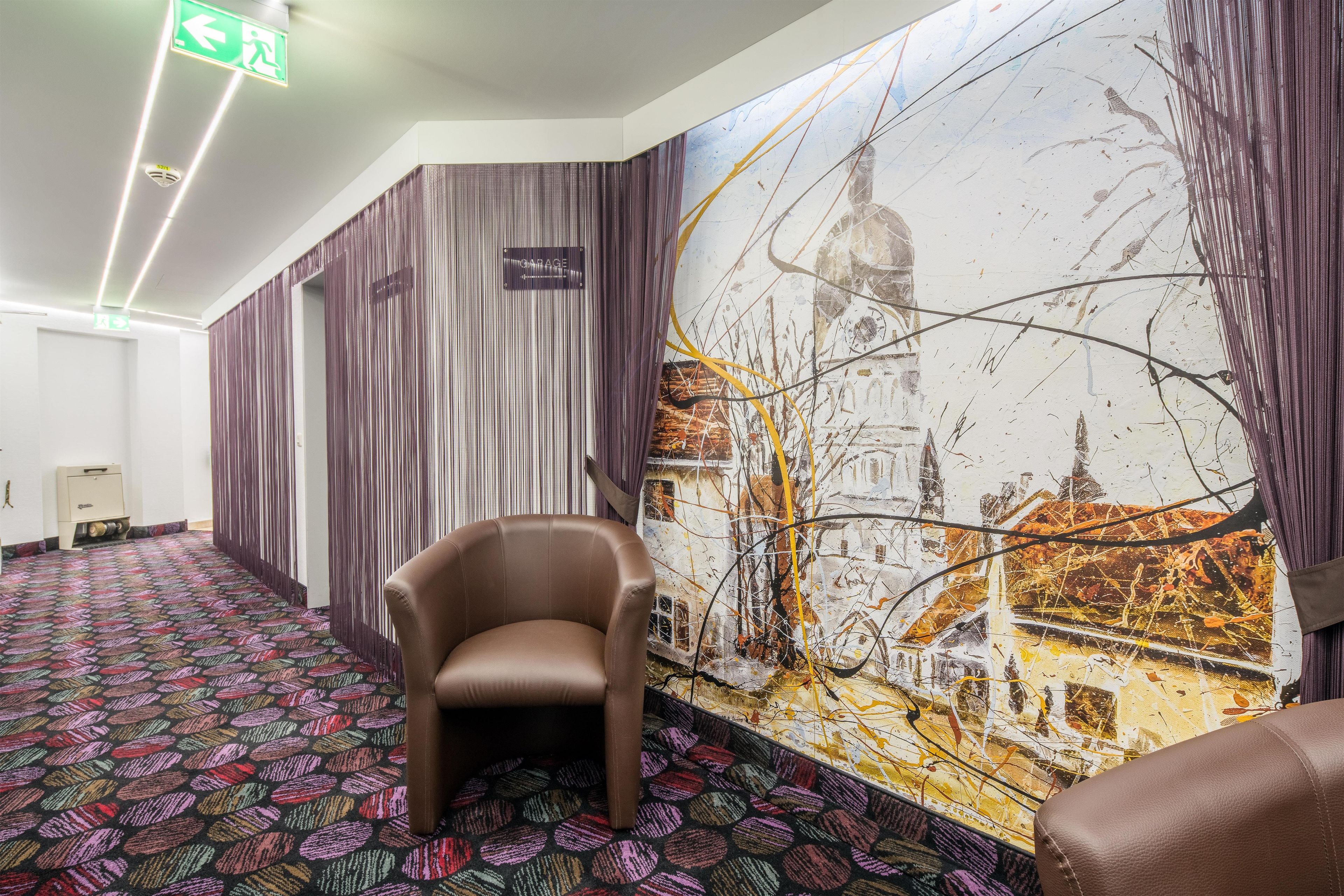 Pasillo de hotel con alfombra estampada, una silla y un mural con vista a un paisaje urbano.