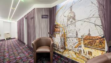 Pasillo de hotel con alfombra estampada, una silla y un mural con vista a un paisaje urbano.