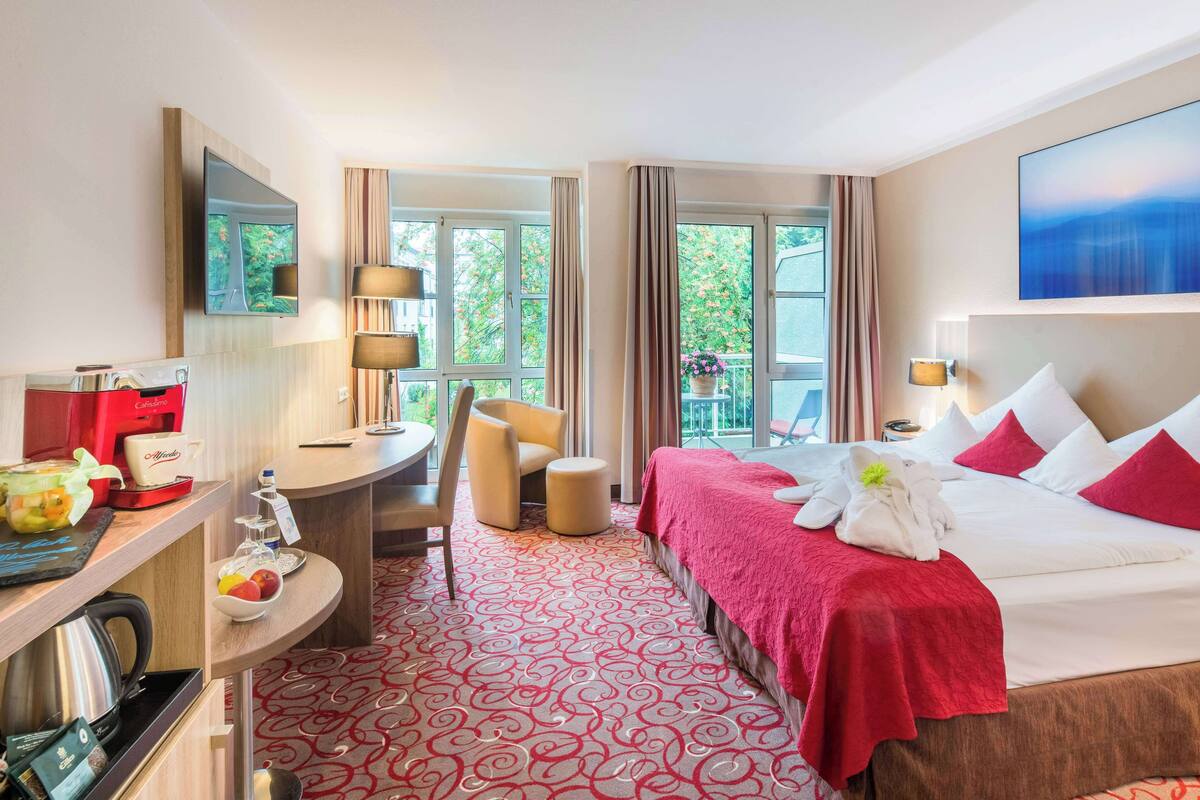 A hotel room with a bed, a desk, a chair, a coffee machine, and a view of the outdoors.