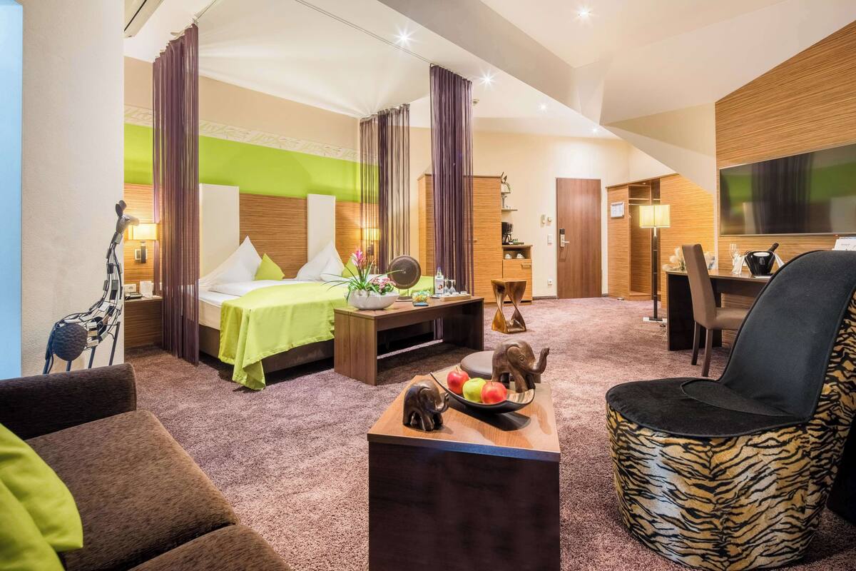 A hotel room with a bed, a desk, a chair, and a small table with fruit and a decorative elephant.