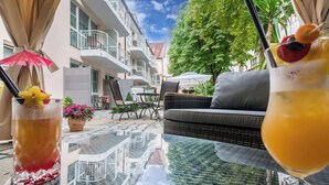 Un espacio al aire libre con mesa de vidrio, mobiliario de mimbre y vistas a un edificio con balcones.