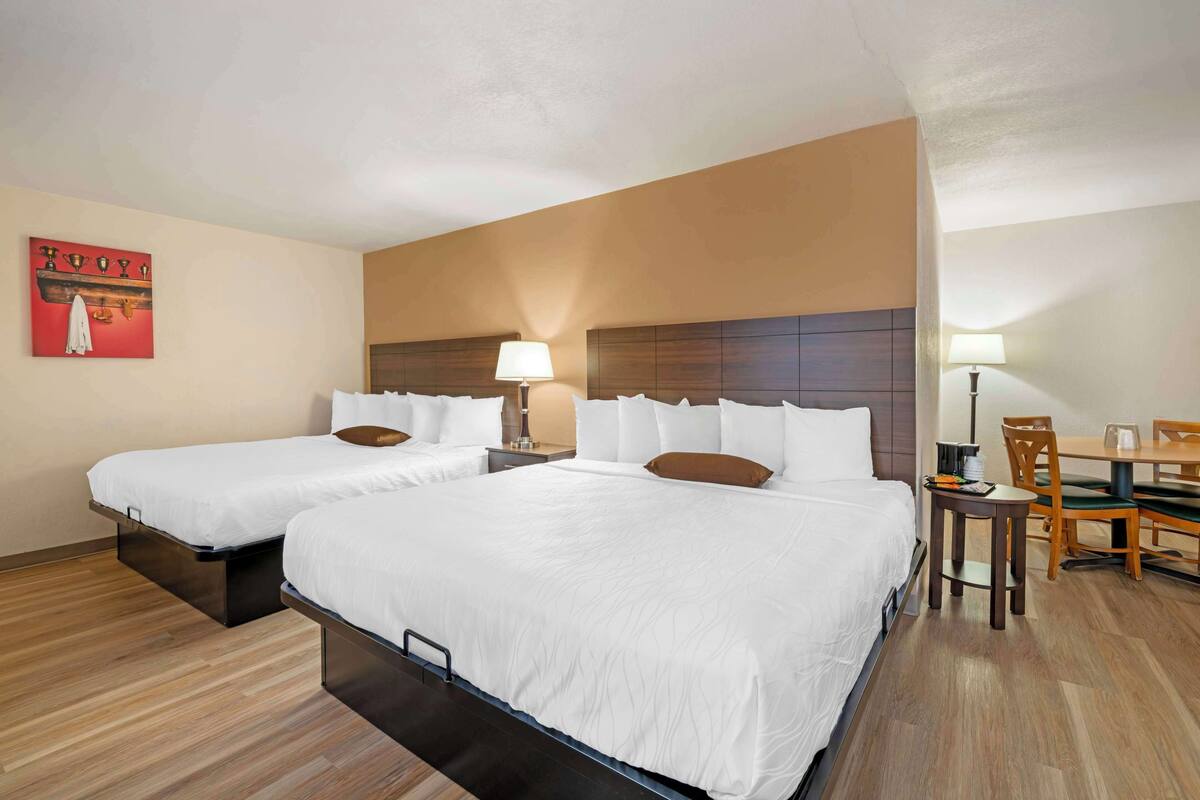 Une chambre d’hôtel avec deux lits, une table à manger, des chaises et une petite table avec une lampe.