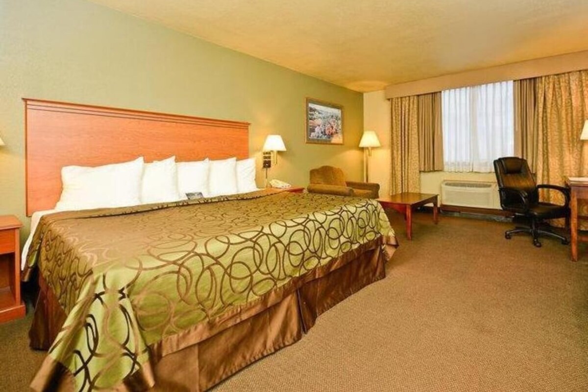 A hotel room with a large bed, a desk, a chair, and a window with curtains.