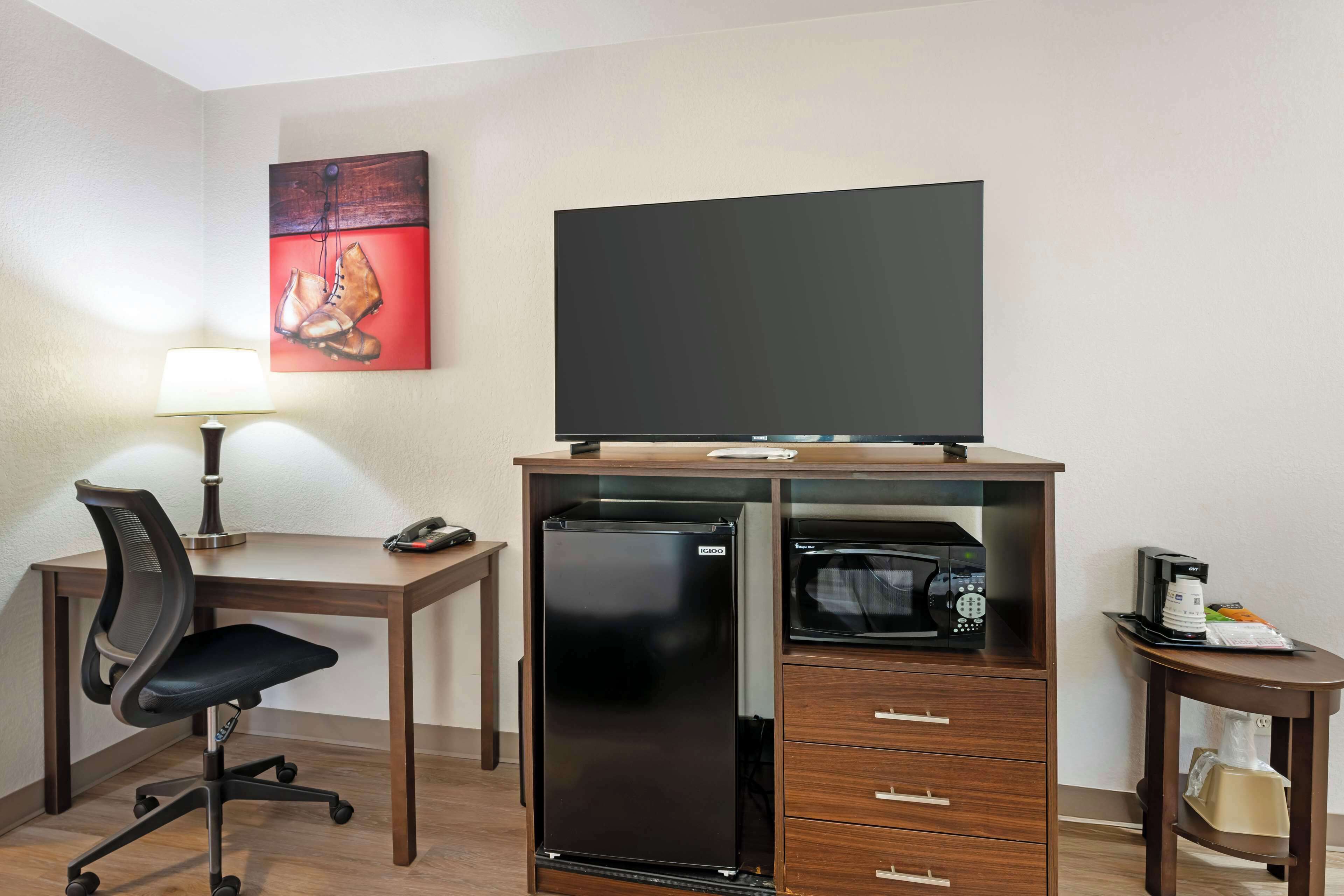 A hotel room with a desk, chair, flat-screen TV, refrigerator, microwave, and a coffee maker.