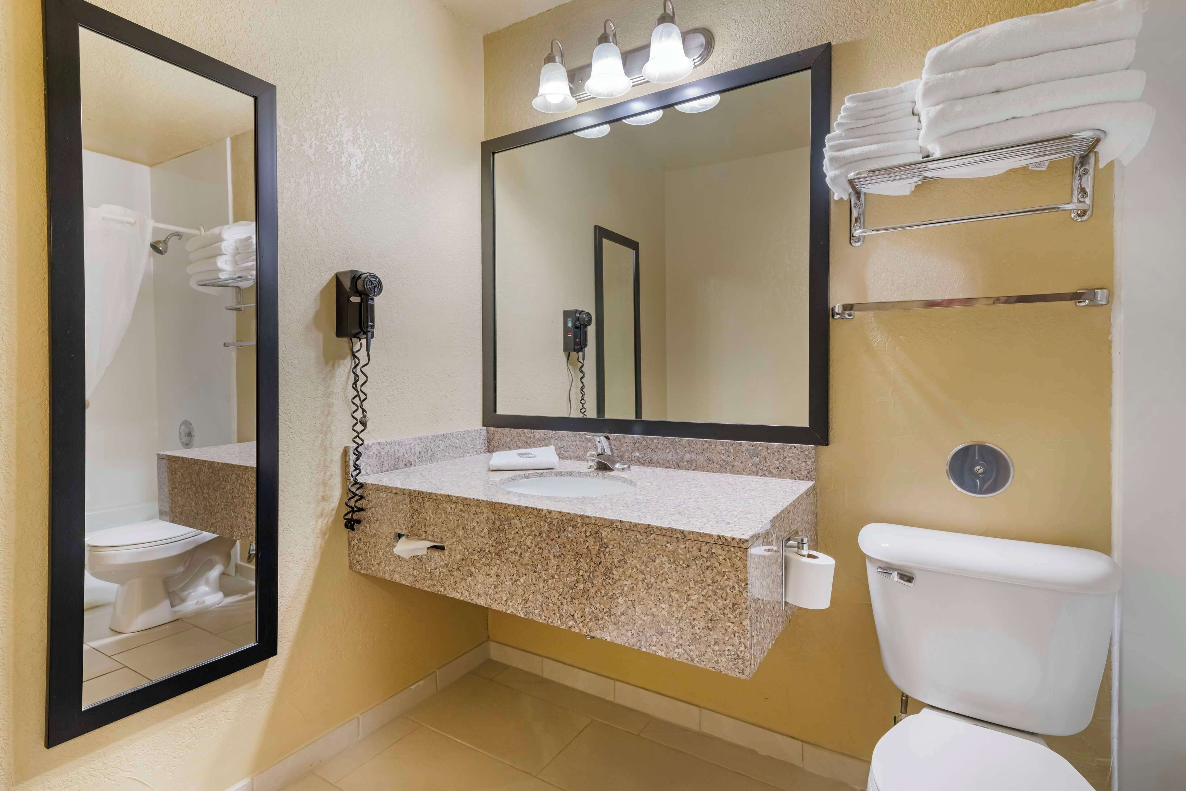A bathroom with a granite countertop sink, a large mirror, a hairdryer, and a towel rack.