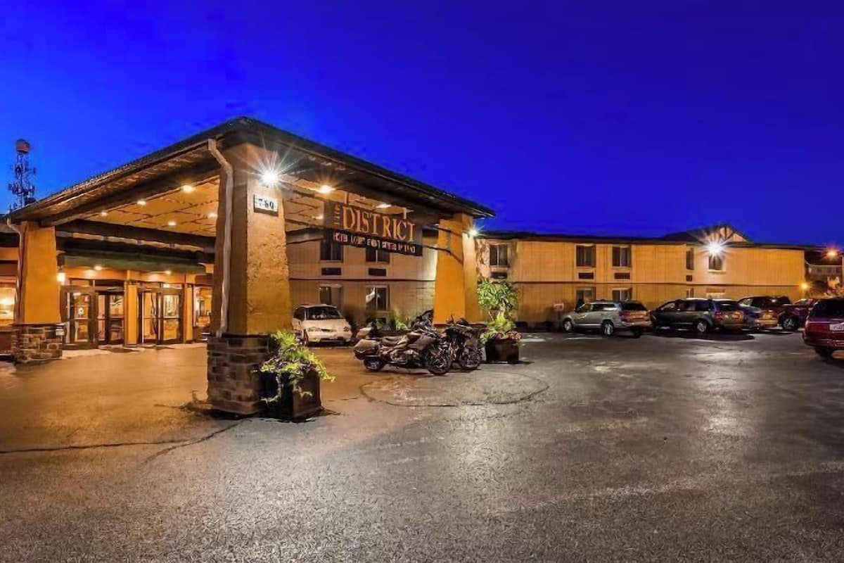A hotel entrance with a covered area, a sign reading 'DISTRICT,' and several parked cars.