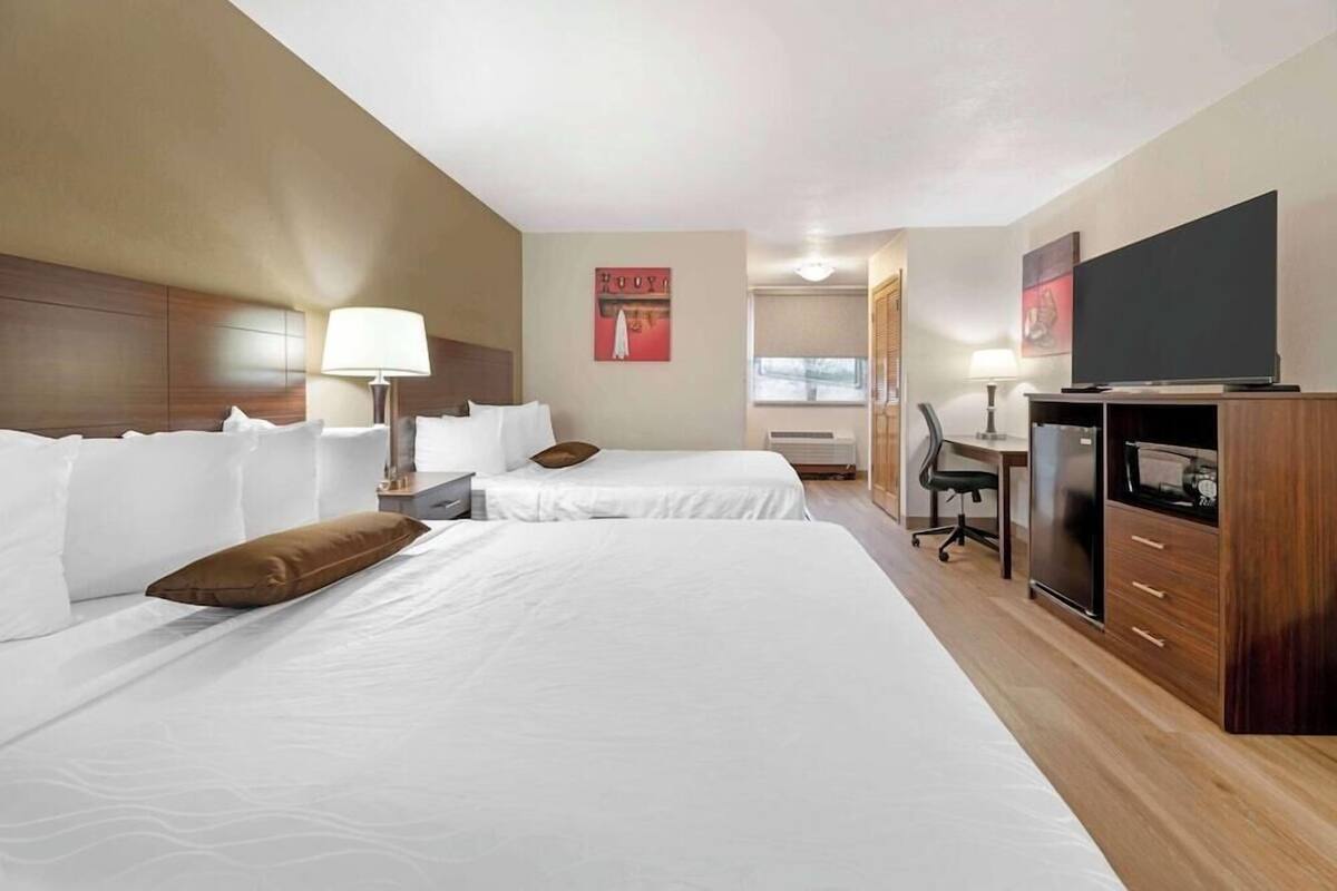 A hotel room with two beds, a desk, a TV, and a minibar.