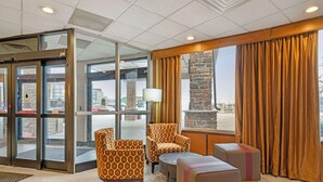 Eine Lobby mit Glastür, gemusterten Sesseln, einem kleinen Tisch und einer Steinsäule.