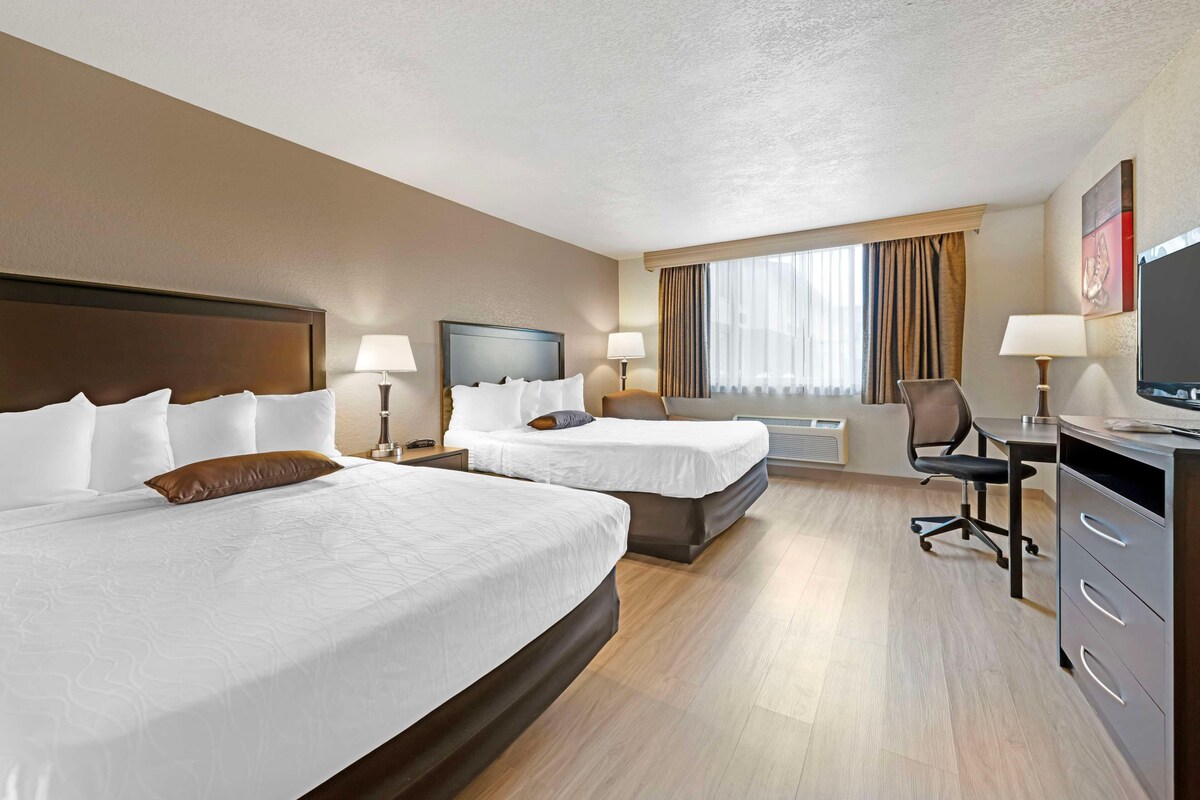 A hotel room with two beds, a desk, a chair, a television, and a window with curtains.