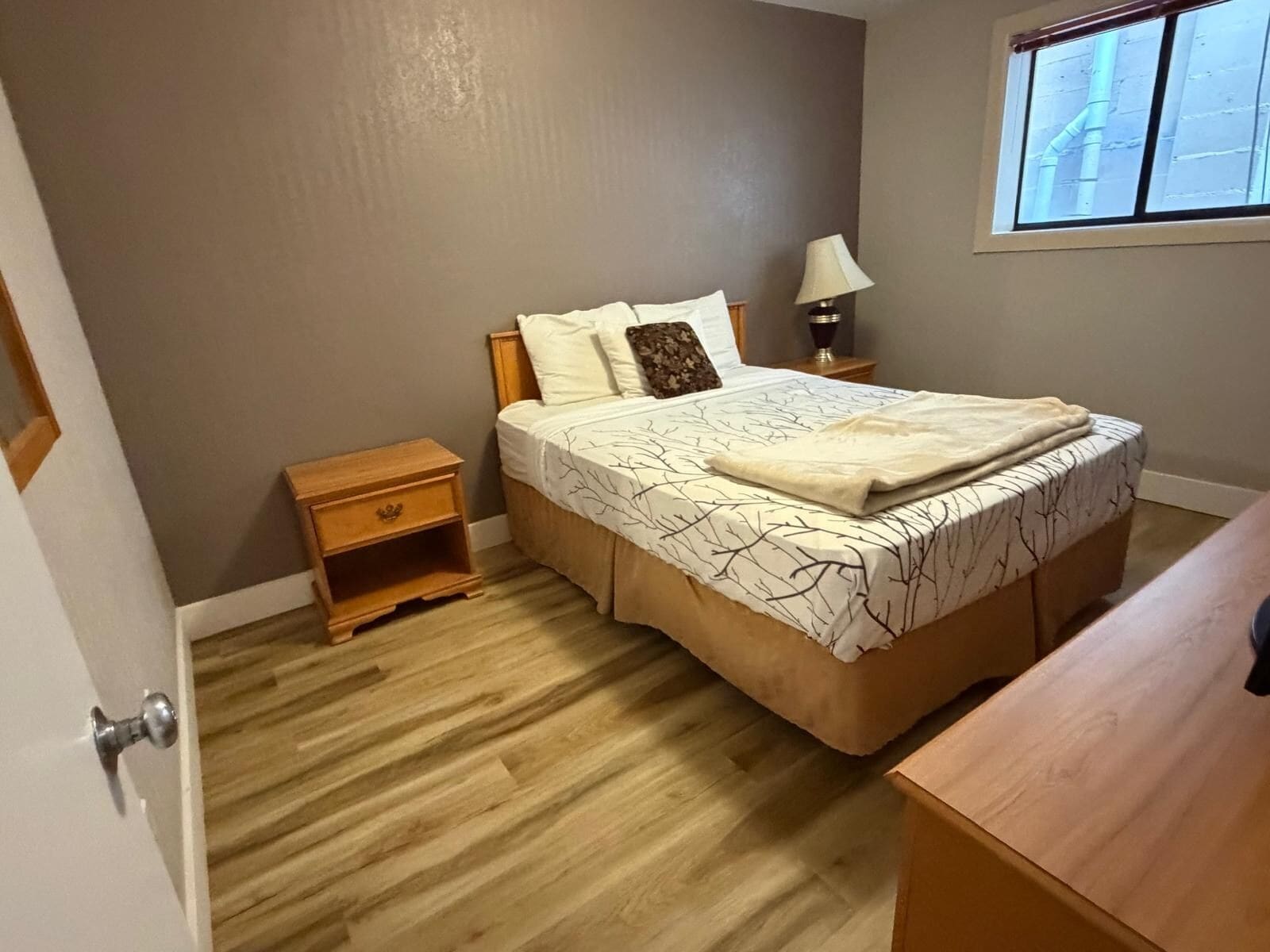 Ein Schlafzimmer mit Bett, Nachttisch, Lampe und Fenster.