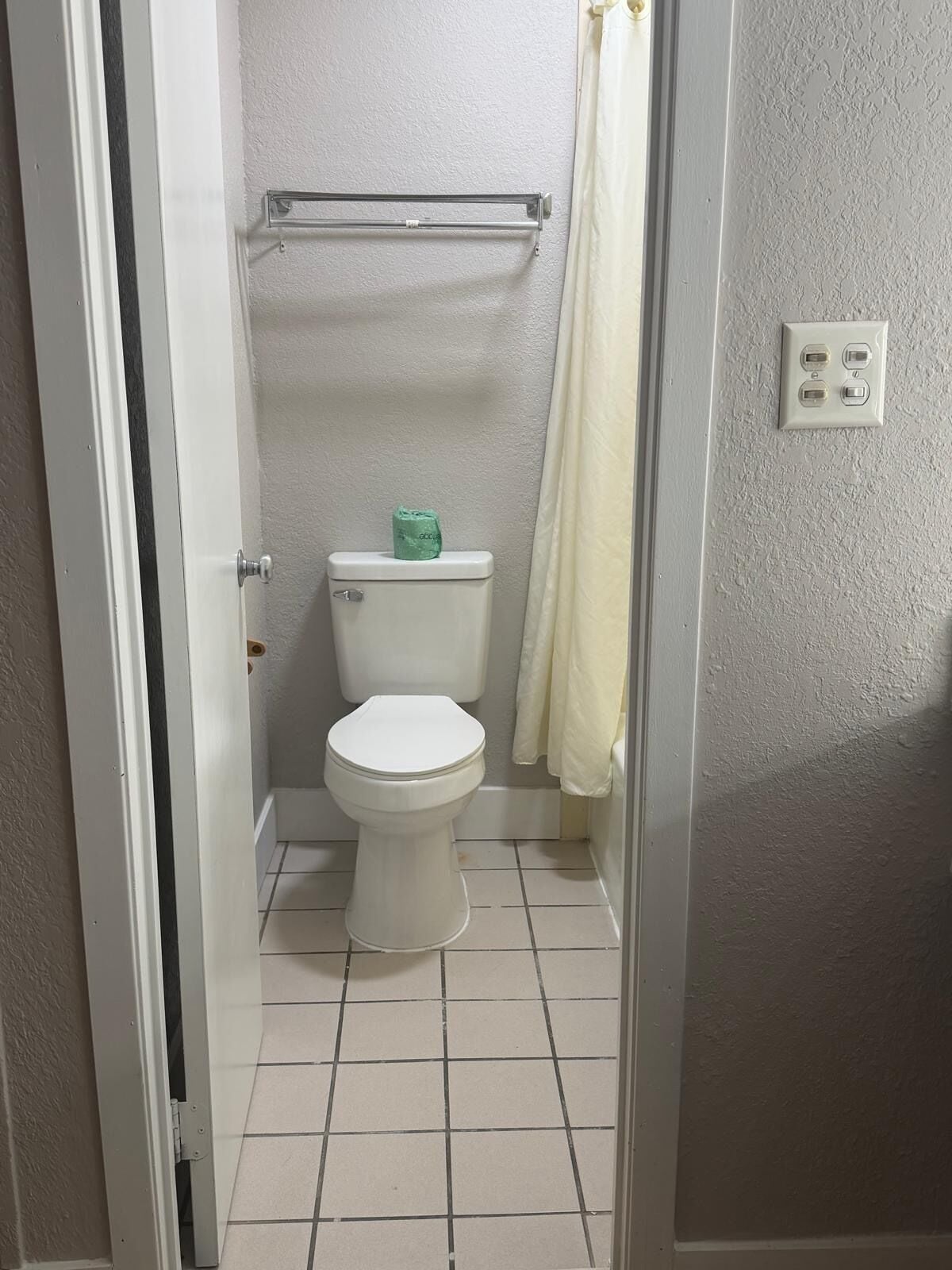 A bathroom with a toilet, a towel rack, and a shower curtain.