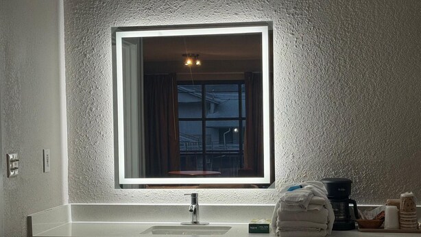 Un baño con lavamanos blanco, un espejo con luz, una ventana y un perchero para toallas.
