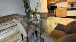 Una sala moderna con una mesa de comedor de vidrio, un sofá color beige y una cocina al fondo.