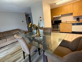 Una sala moderna con una mesa de comedor de vidrio, un sofá color beige y una cocina al fondo.
