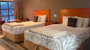 Habitación de hotel con dos camas, una mesita, una silla y una ventana con cortinas.