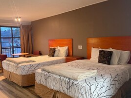 Habitación de hotel con dos camas, una mesita, una silla y una ventana con cortinas.