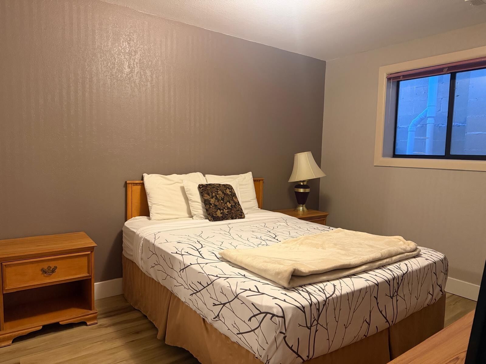 Un dormitorio con cama, mesitas de noche, lámpara y ventana.