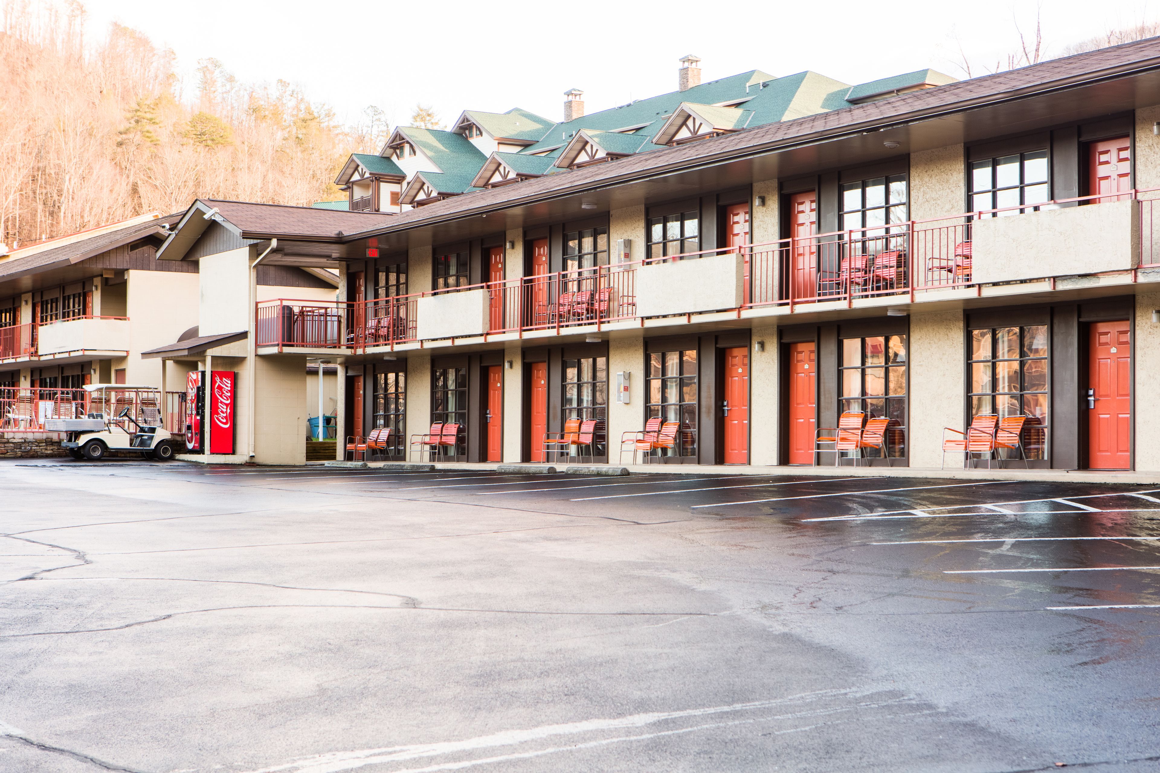Een motel met meerdere verdiepingen, een Coca-Cola bord, terras en een parkeerplaats.