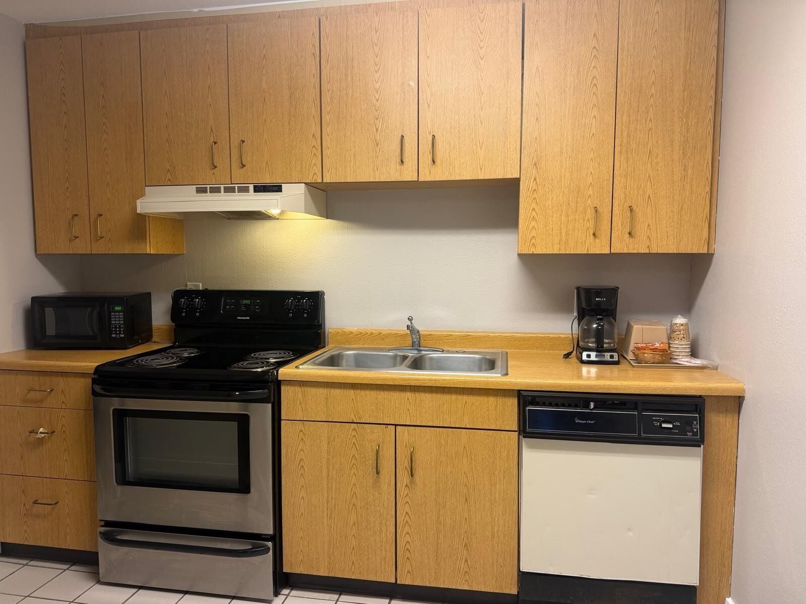 A compact kitchen with wooden cabinets, a microwave, a stove, a sink, and a dishwasher.