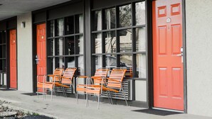 Un edificio con puertas y ventanas anaranjadas, mobiliario exterior con sillas color naranja, y fachada de hormigón.