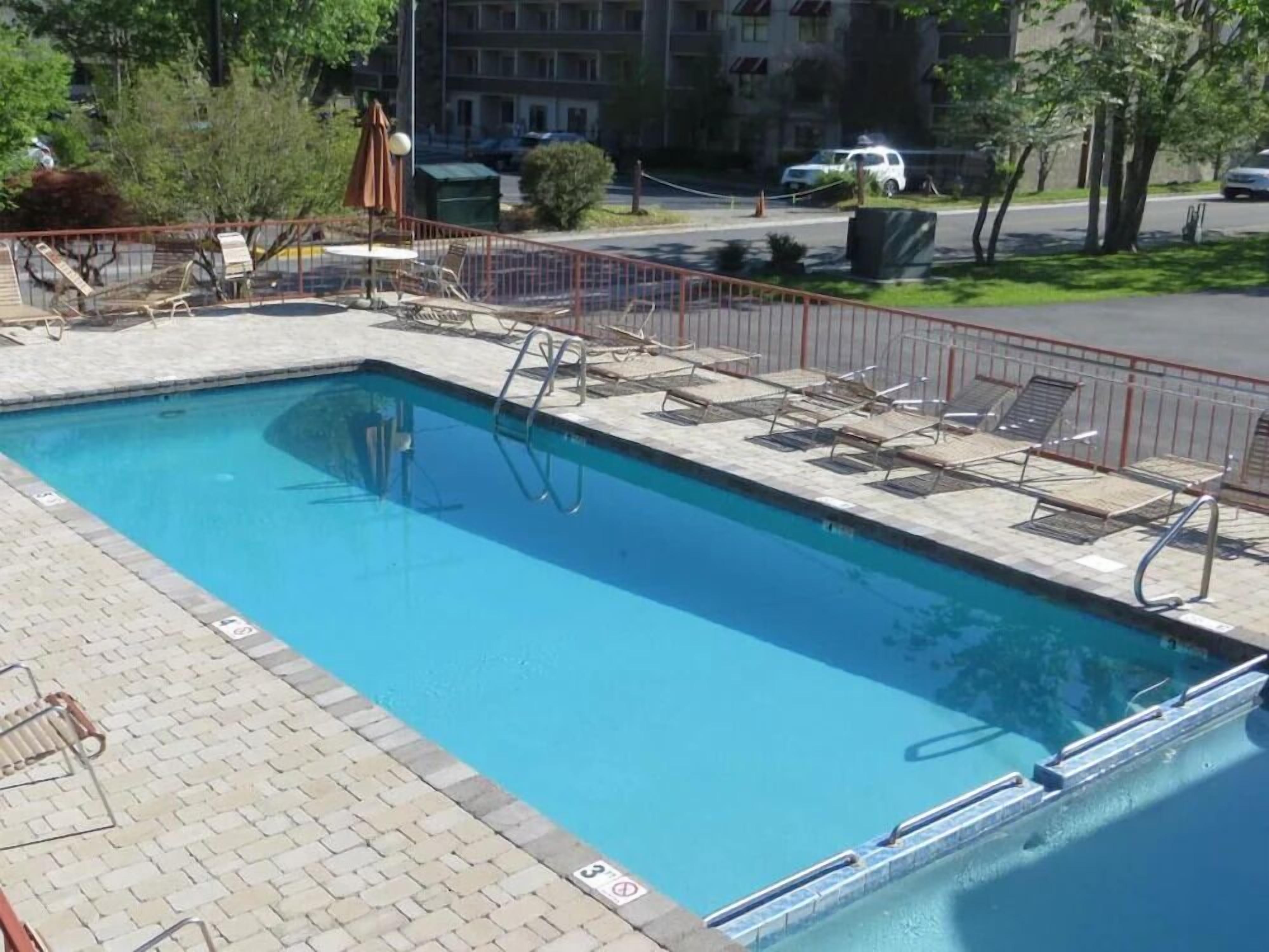 A rectangular swimming pool with a tiled deck, surrounded by a metal fence.