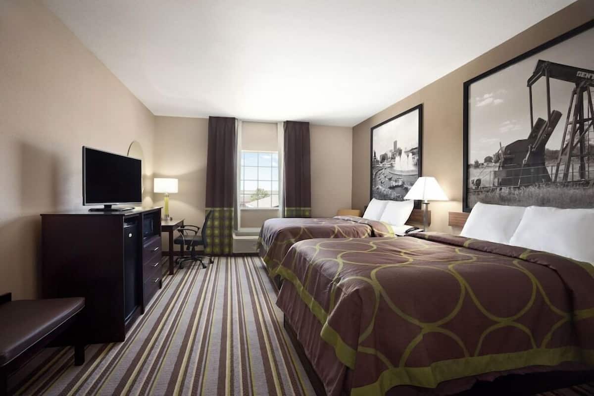 Ein Hotelzimmer mit zwei Betten, einem Schreibtisch, einem Fernseher und einem Vorhangfenster.