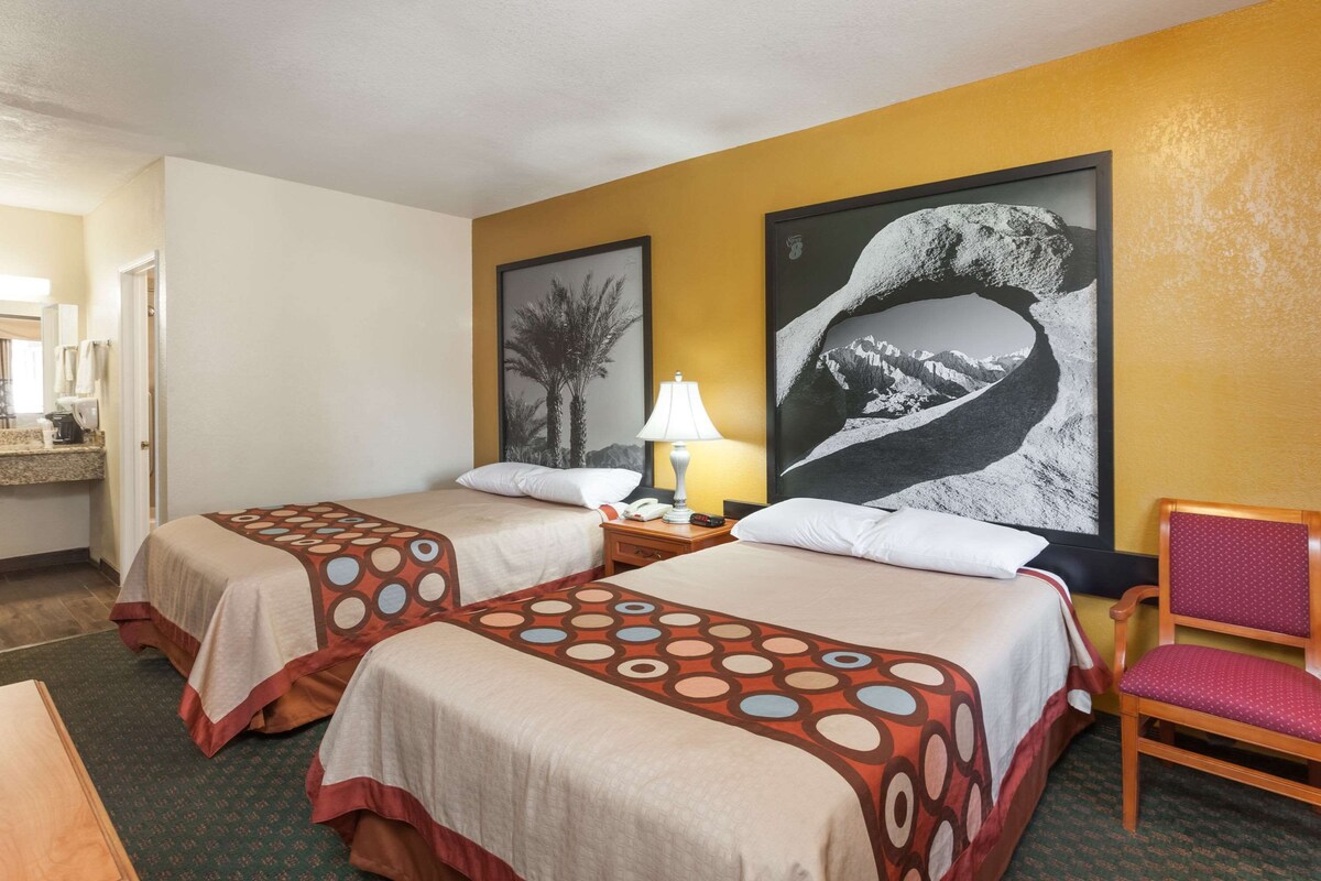 A hotel room with two beds, a desk, a chair, and two large framed pictures on the wall.